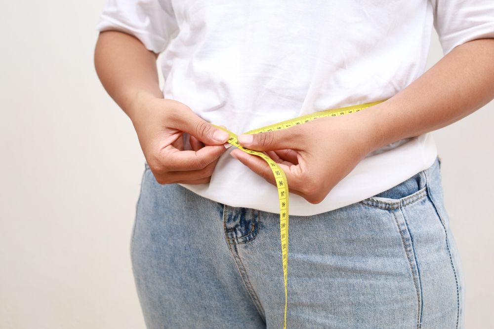 A woman is measuring her waist with a tape measure.