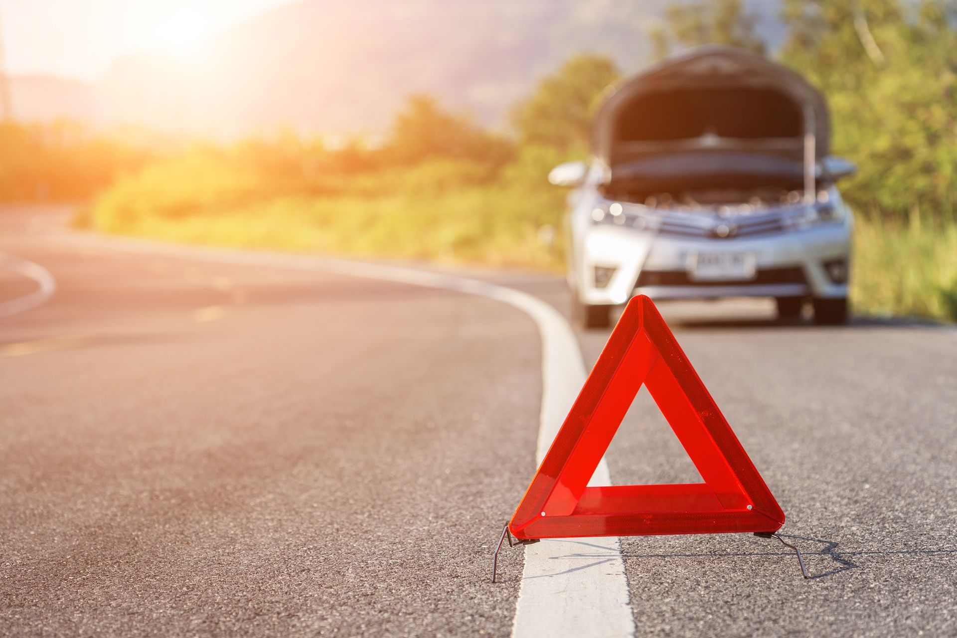 Red warning triangle on a road shoulder with a car stopped in the background at sunset Red warning triangle on a road shoulder with a car stopped in the background at sunset