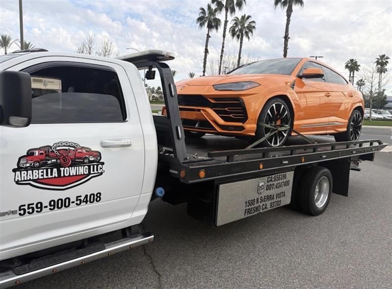 Tow truck hauling an orange SUV on a flatbed in a palm-lined parking lot