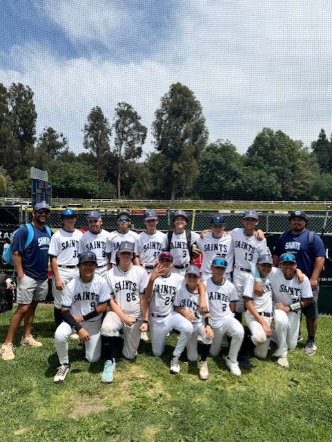Youth baseball team posing on a grassy field in white uniforms, with coaches at the sides.
