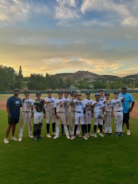 Youth baseball team posing on a grassy field at sunset with mountains in the background.