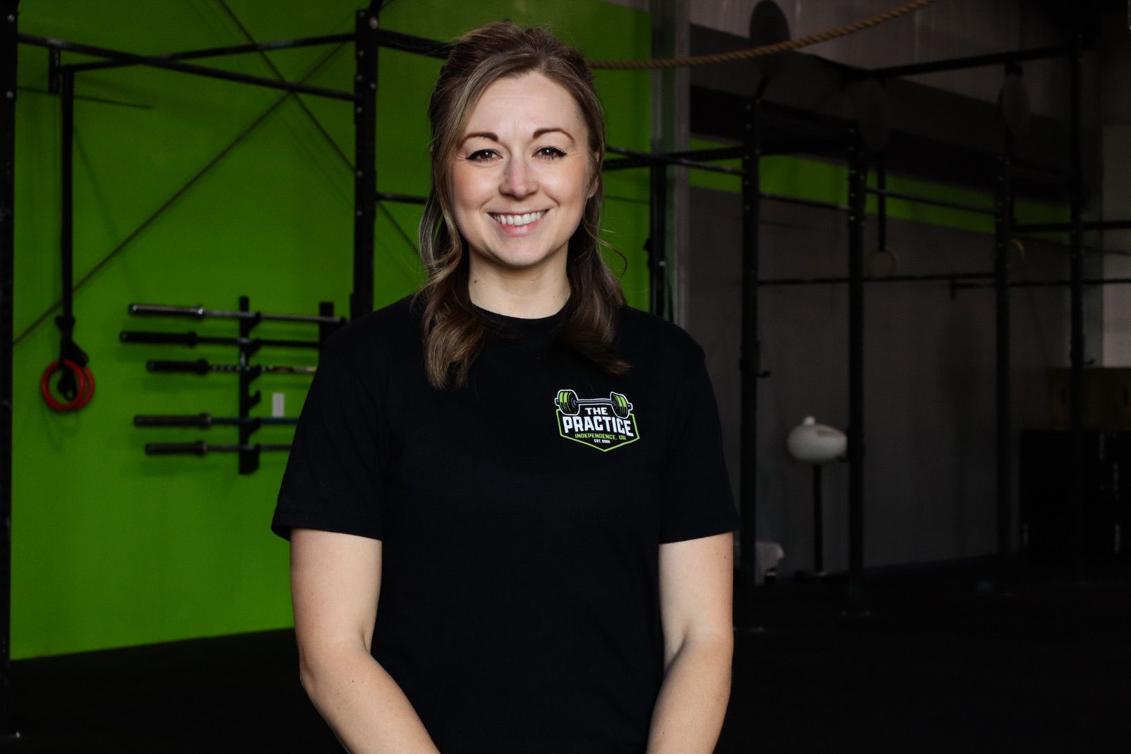 Woman in workout clothes leans against a weight rack in a gym, smiling.