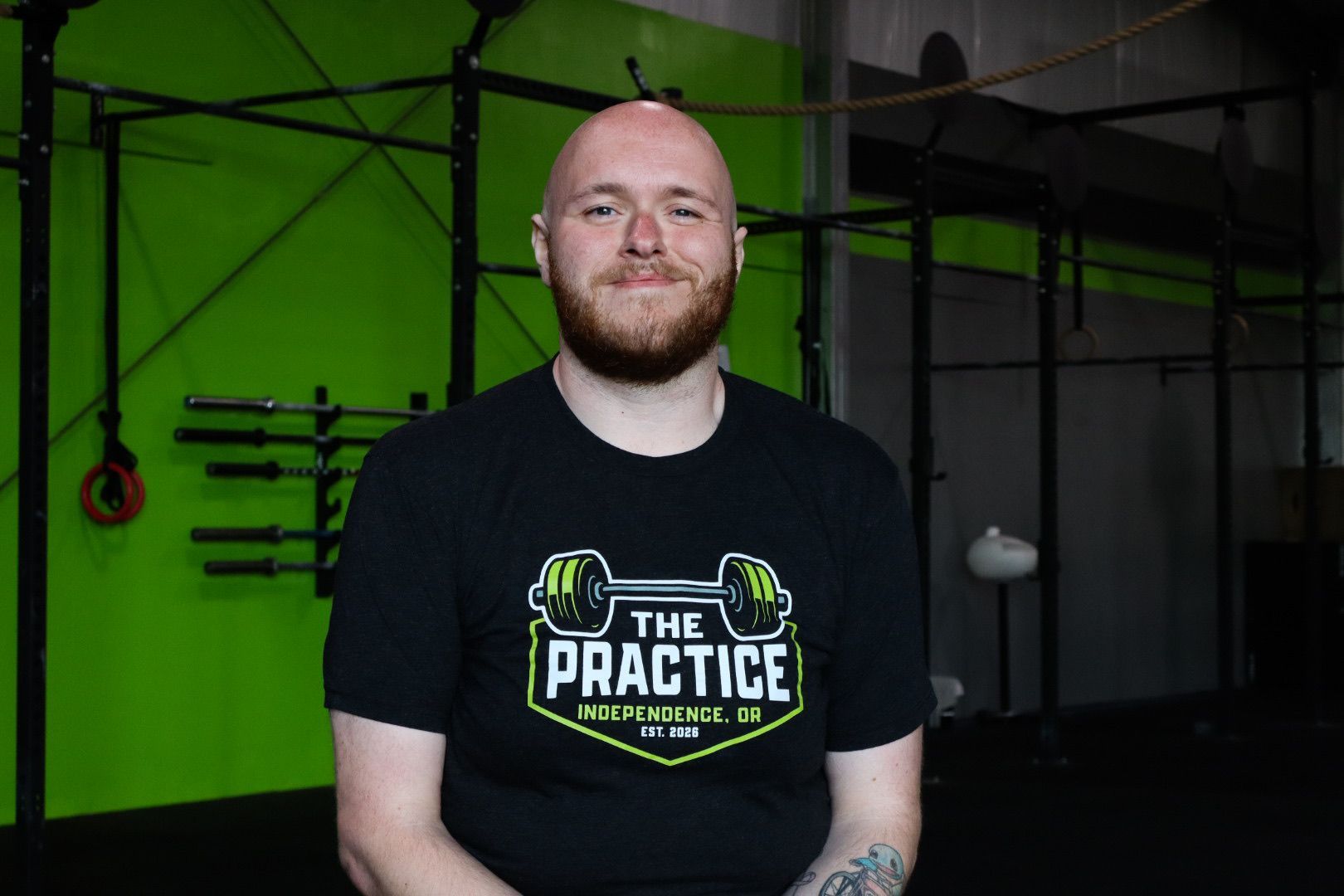 Man with a beard in a gym, wearing a black shirt that says 