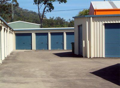 Storage units with blue doors and metal siding, situated on a concrete lot. Sunny day.