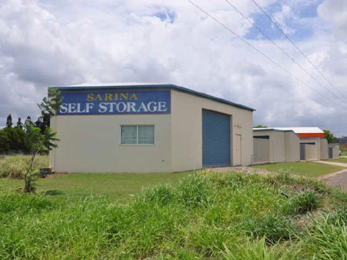 Sarina Self Storage facility with beige buildings, blue roller door, and signage under a cloudy sky.