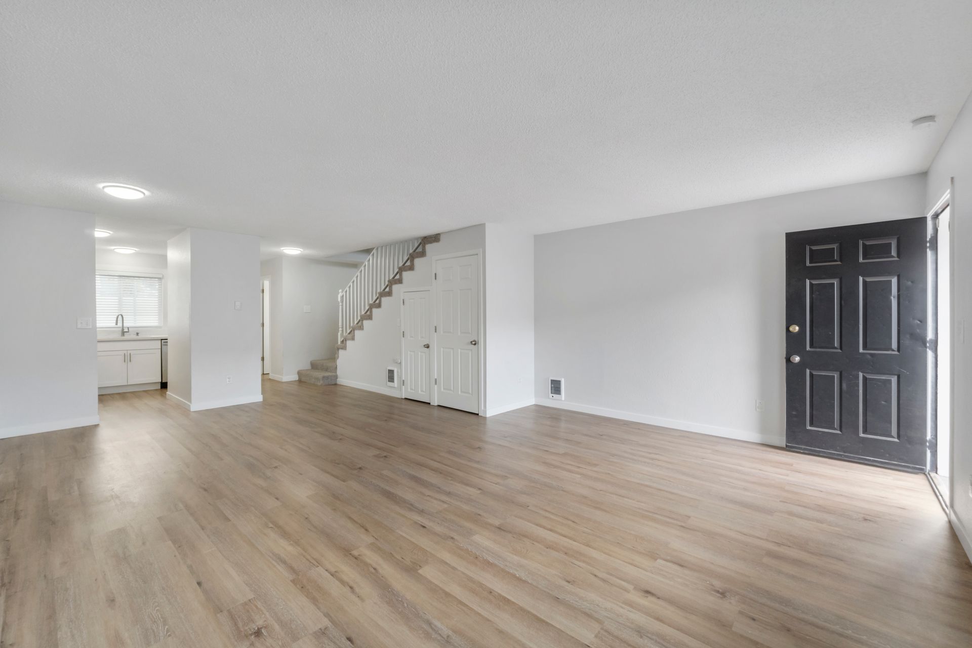An empty living room with hardwood floors and a black door.