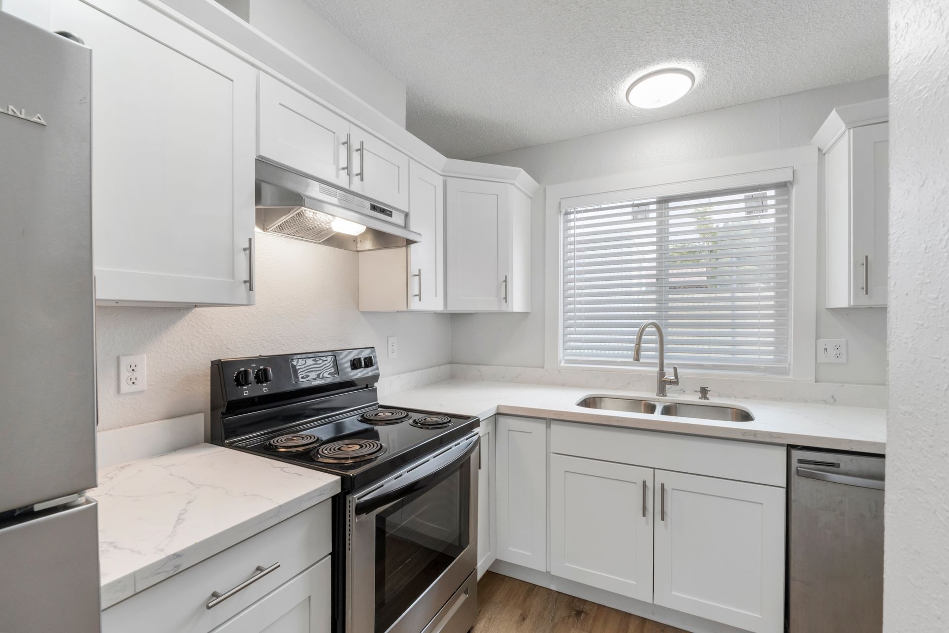 A kitchen with white cabinets , a stove , a refrigerator , a sink , and a window.