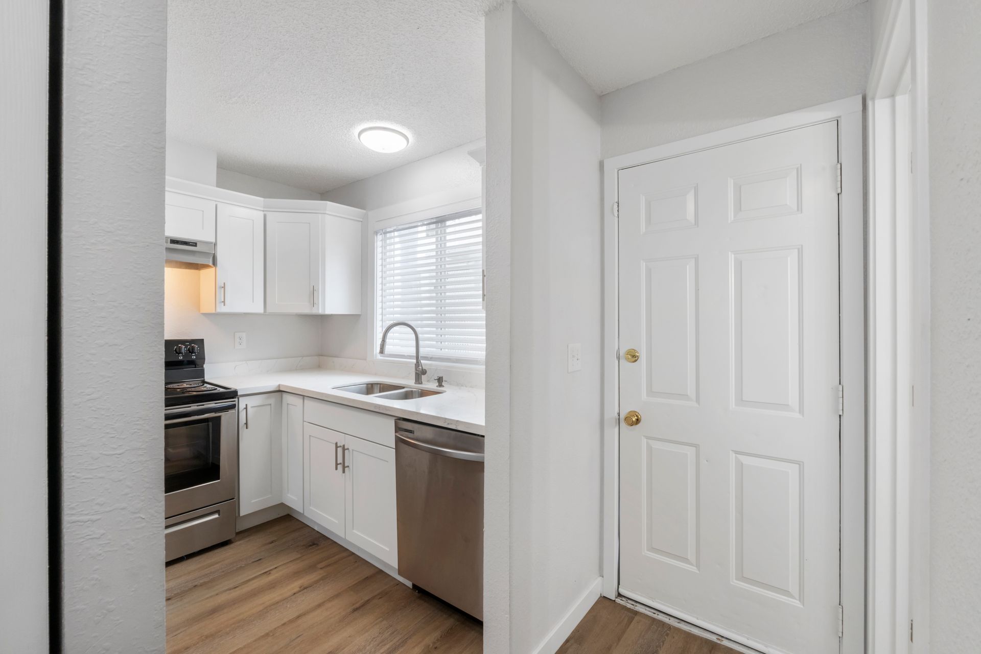 A kitchen with white cabinets , stainless steel appliances , a sink , and a door.