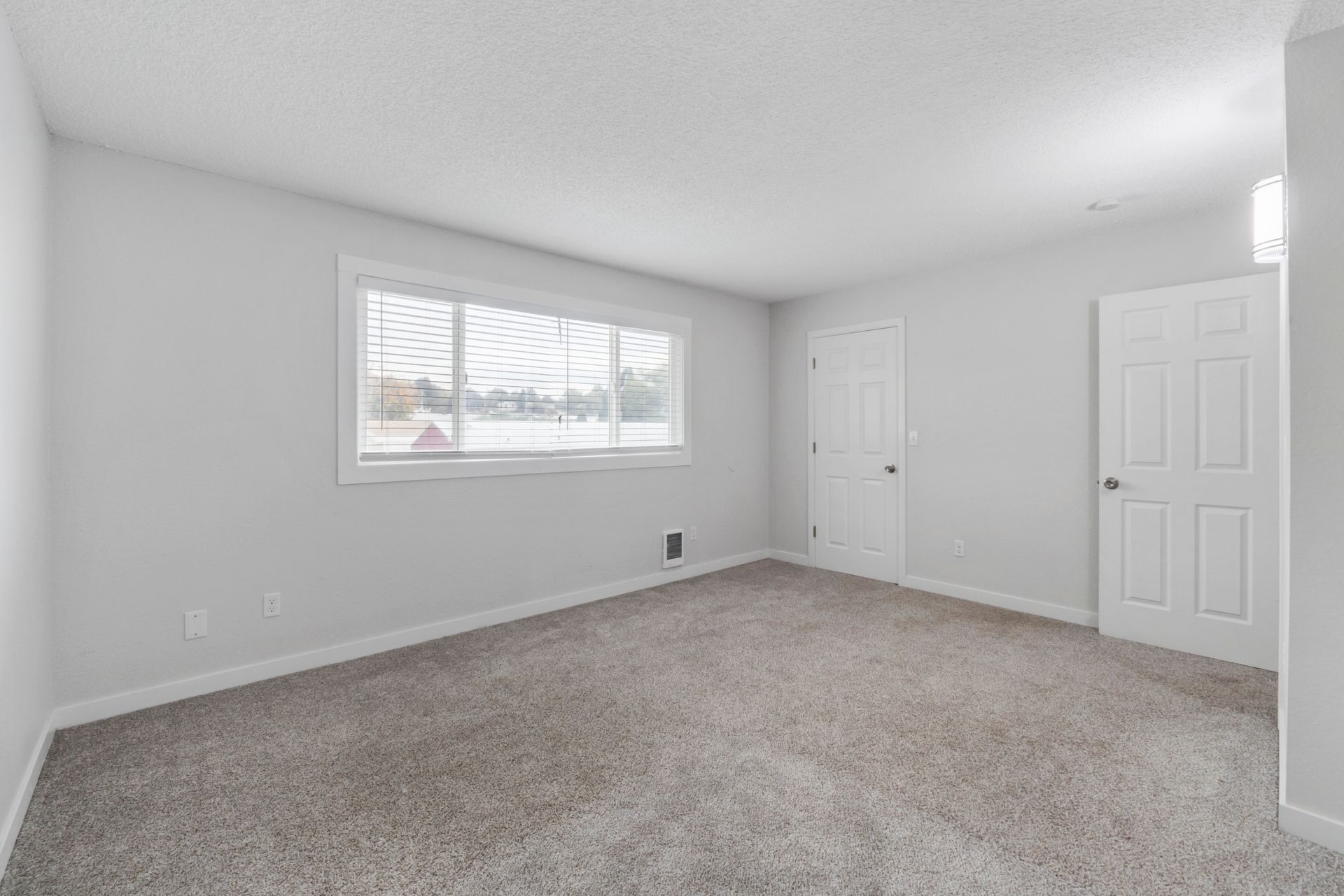 An empty bedroom with a window and a carpeted floor.