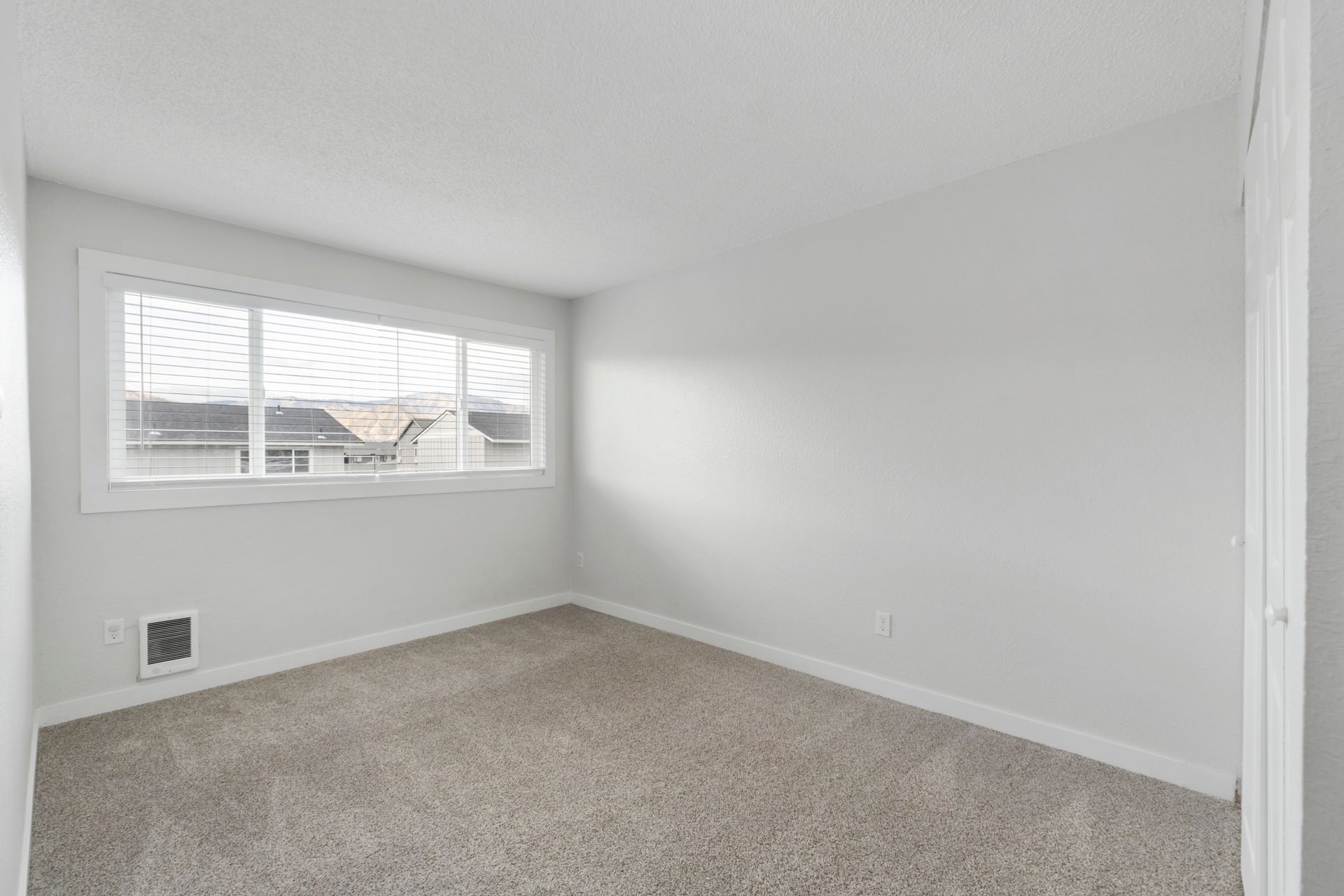 An empty bedroom with a window and carpet.