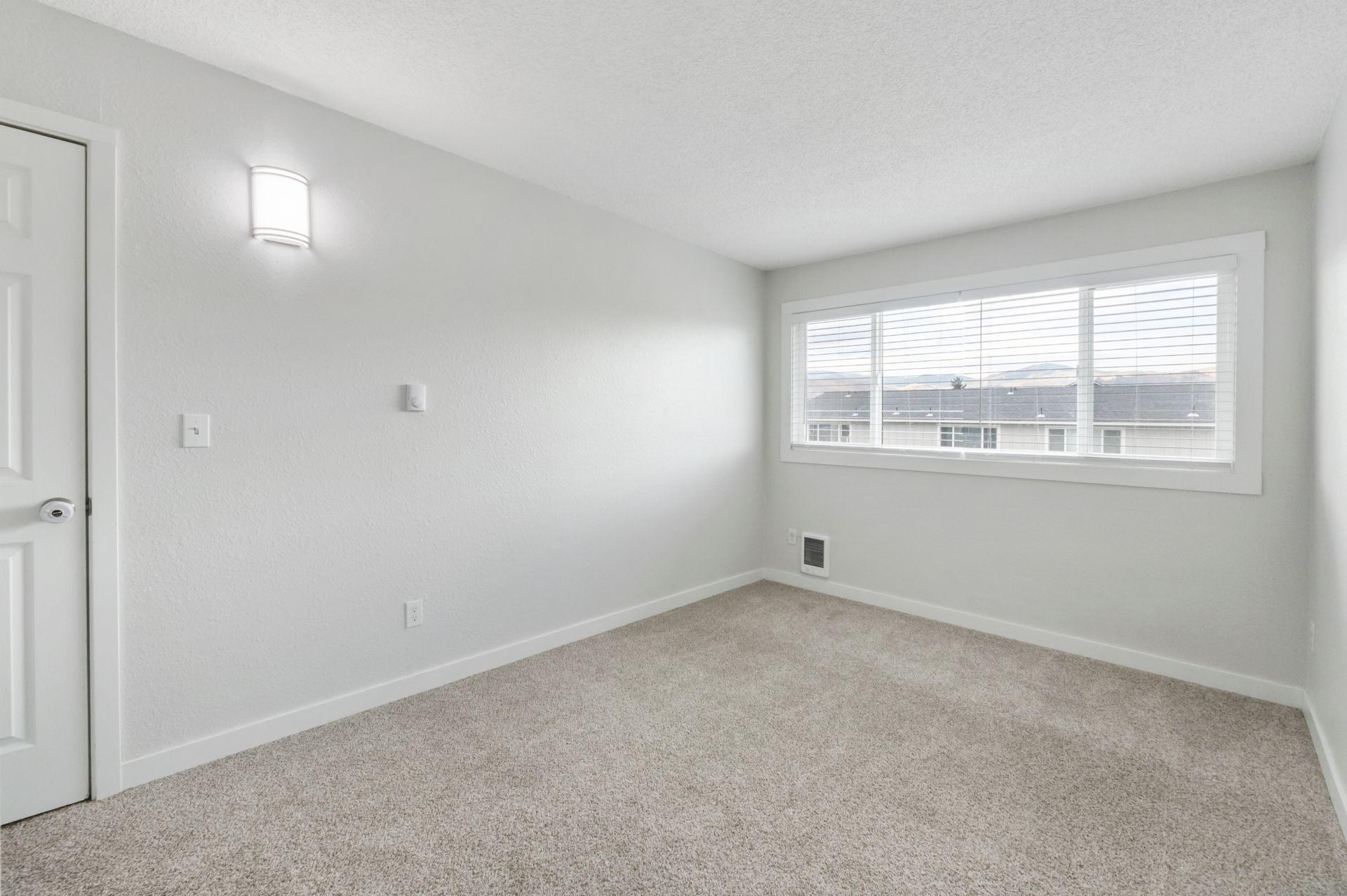 An empty bedroom with a window and a carpeted floor.