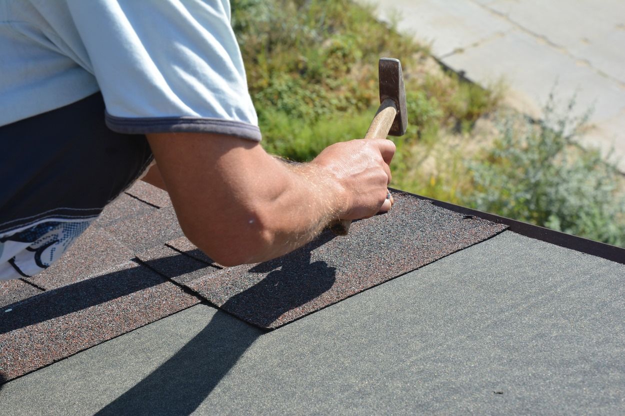 Worker hammering shingles on a roof edge