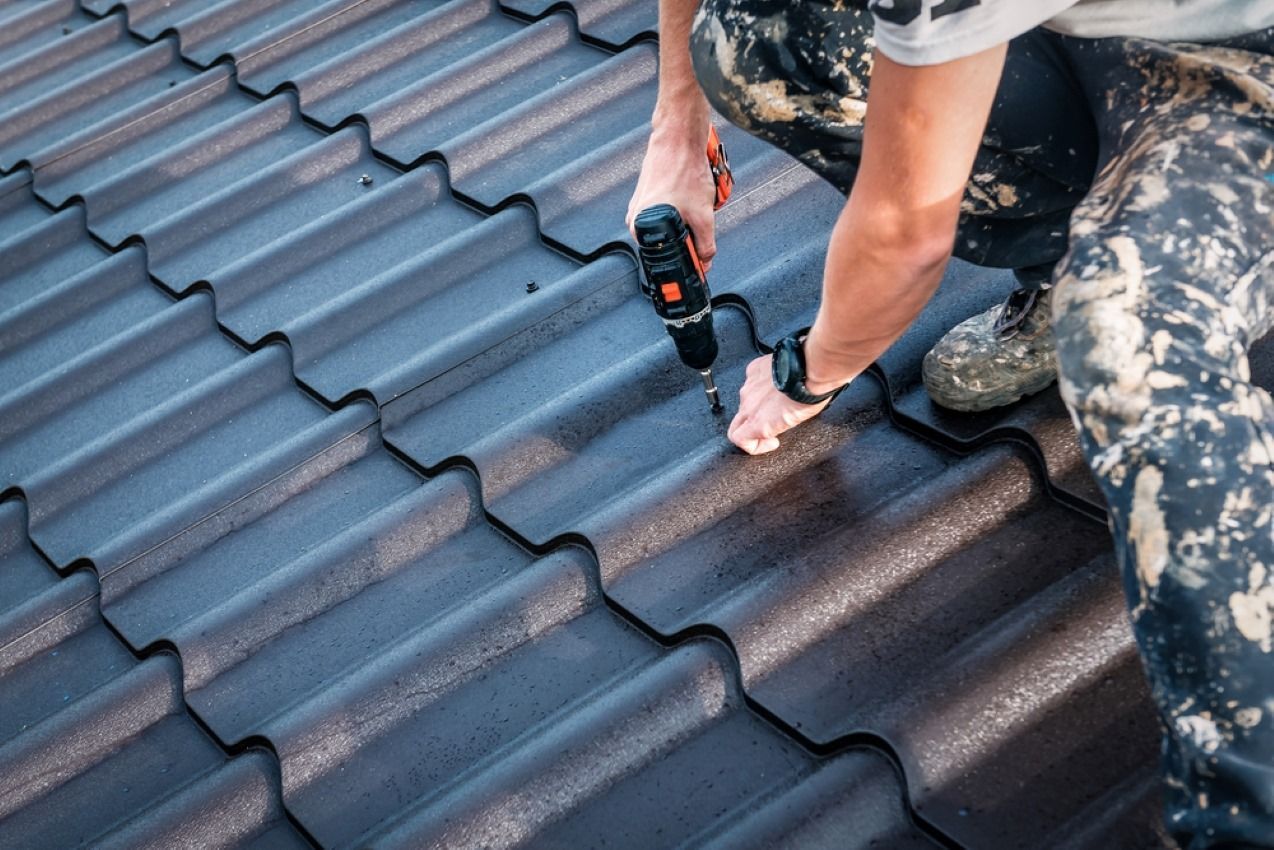 Worker installing dark roof tiles with a power drill on a tiled roof