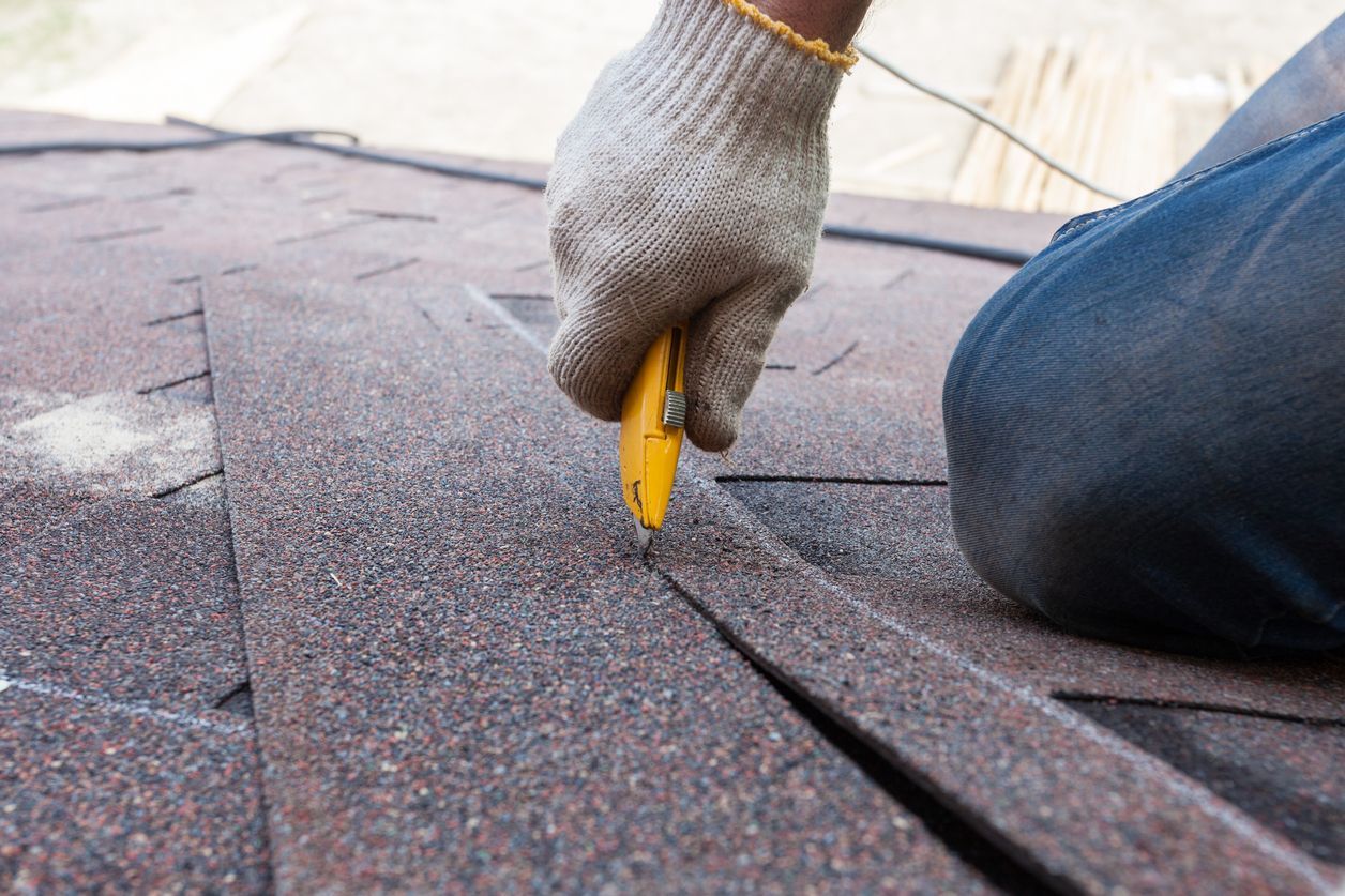 Gloved hand using a utility knife to cut roofing shingles on a rooftop