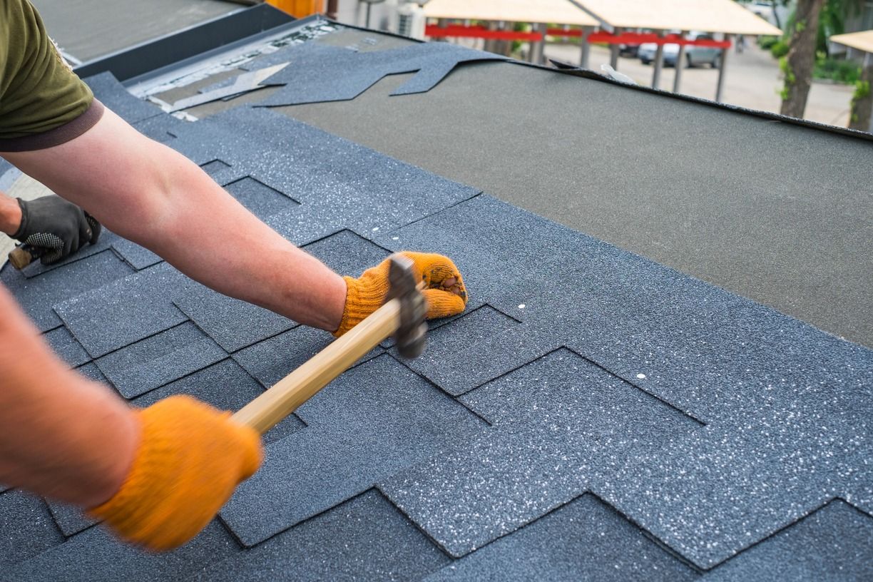 Worker hammering asphalt shingles on a roof