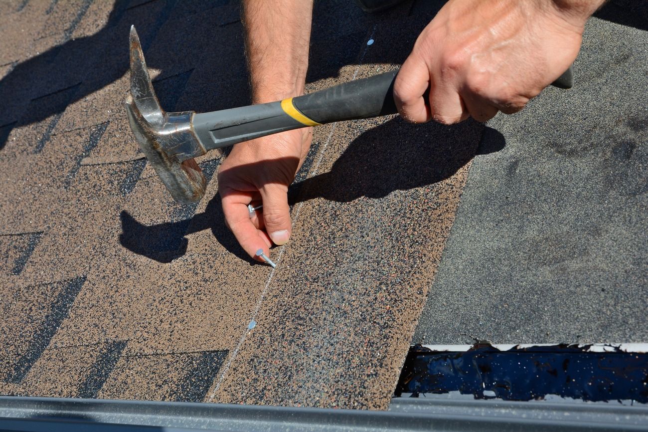 Hands using a hammer to lift shingles on a roof during repair work