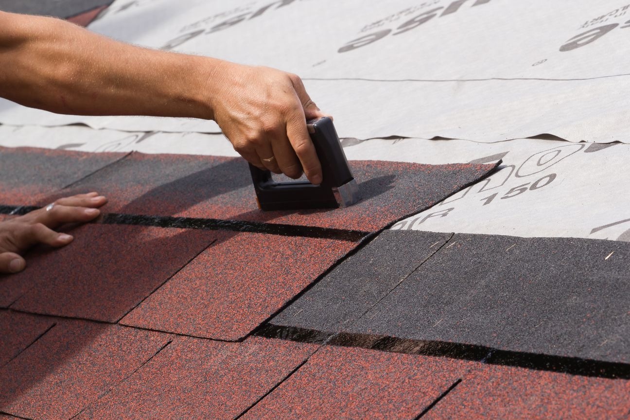 Hand placing a black tool on a red roof shingle during roofing work