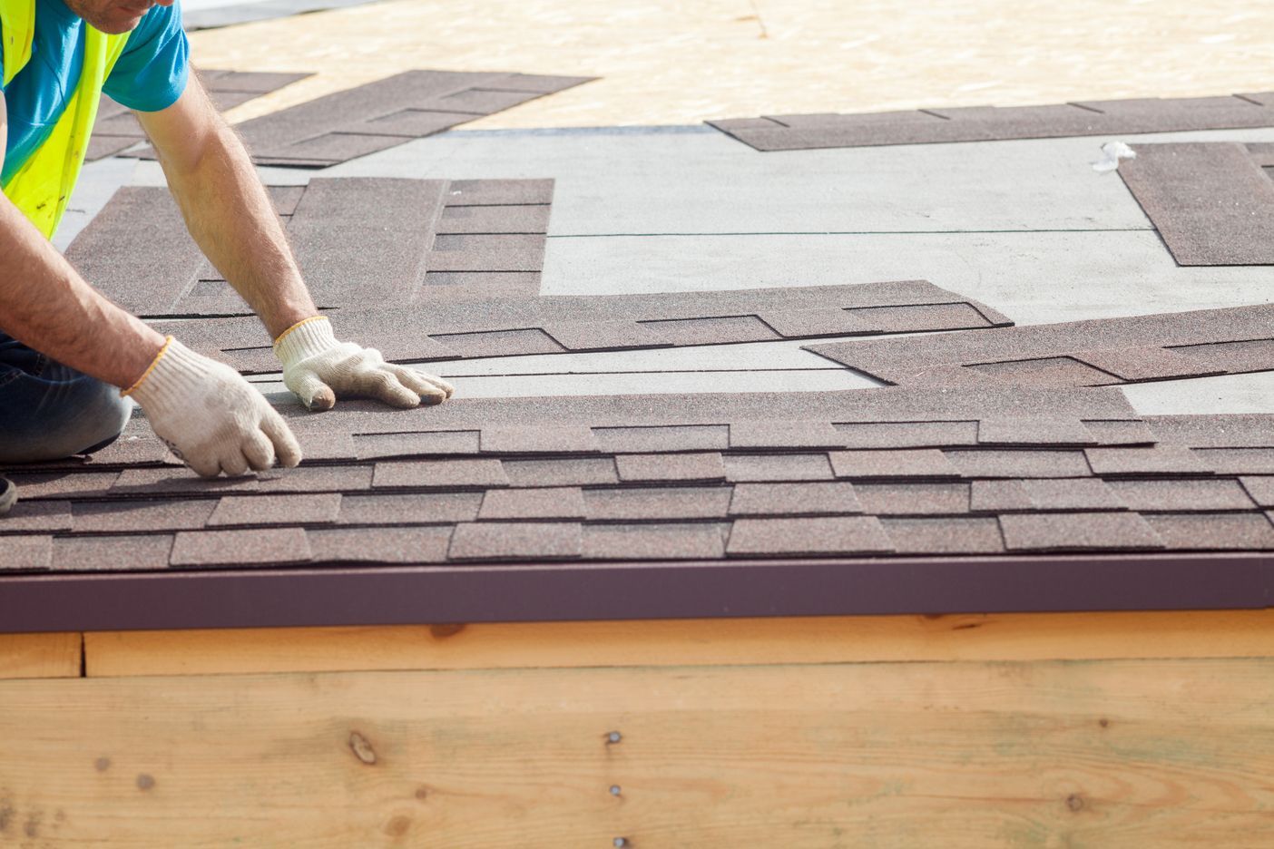 Worker laying gray roof shingles on a wooden roof deck