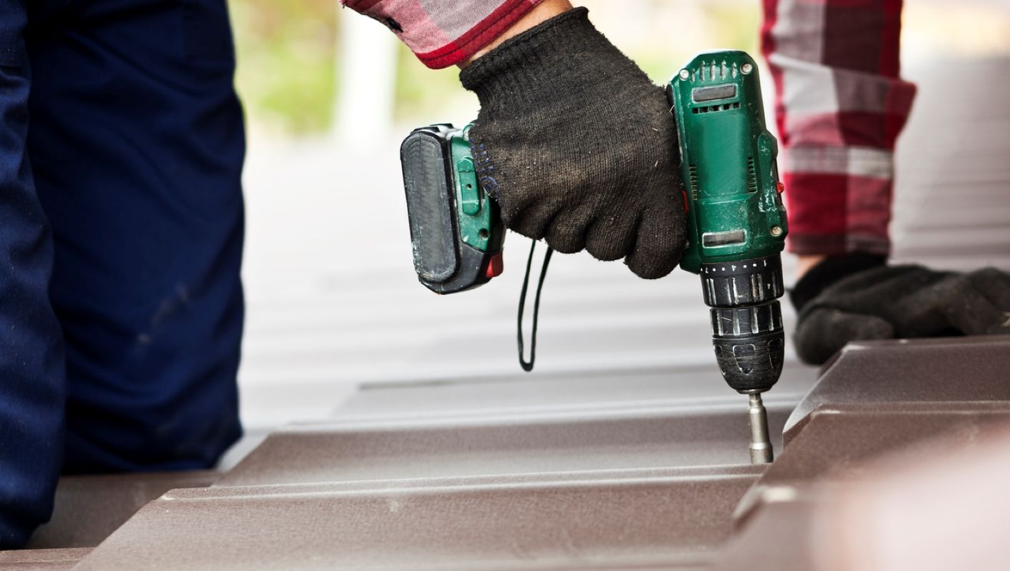 Gloved hand using a green drill to fasten decking boards outdoors