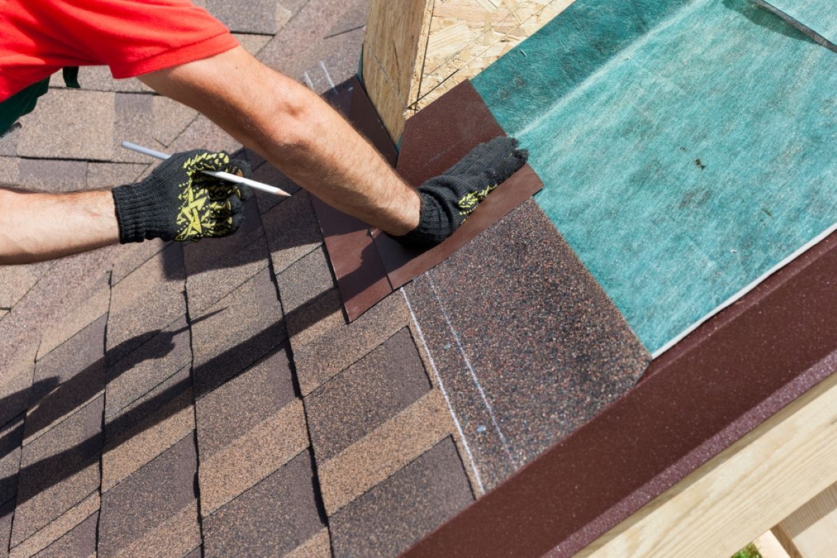 Worker installing shingles on a roof beside a turquoise underlayment sheet