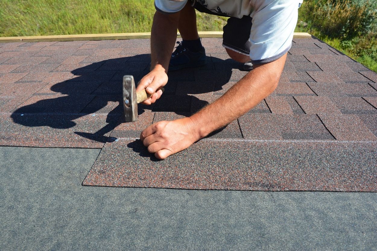 Person hammering roofing shingles on a roof under sunlight