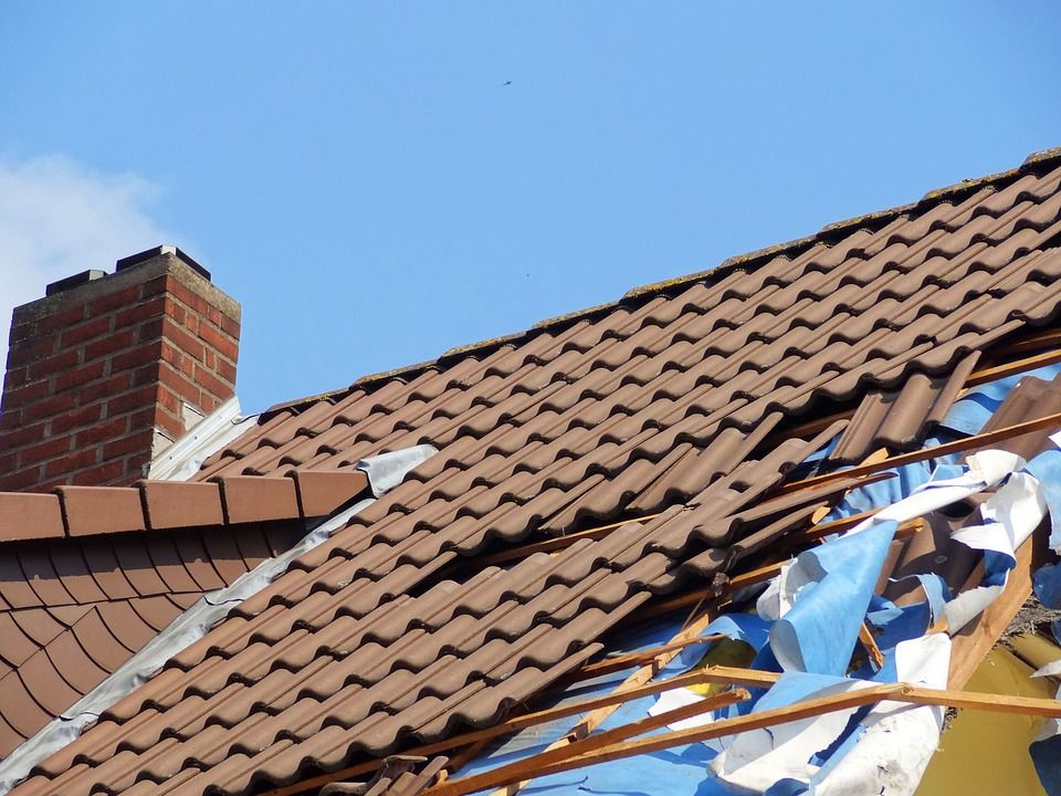 Damaged terracotta roof with broken tiles and exposed wooden beams near a brick chimney