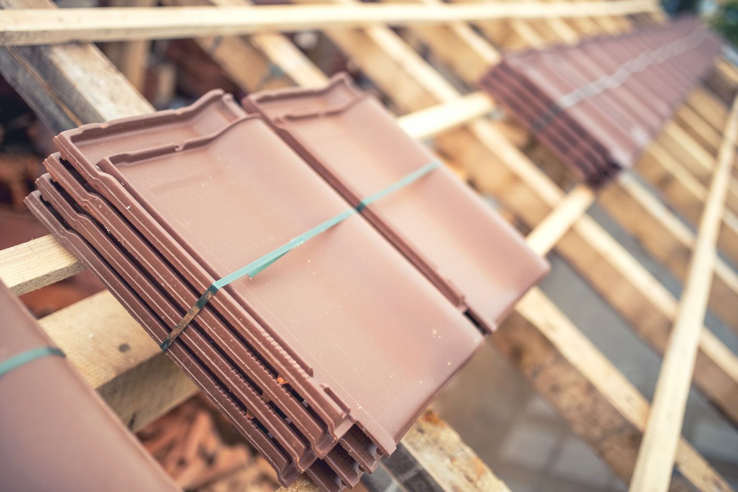 Stacked brown roof tiles tied with blue straps on a wooden rack outdoors