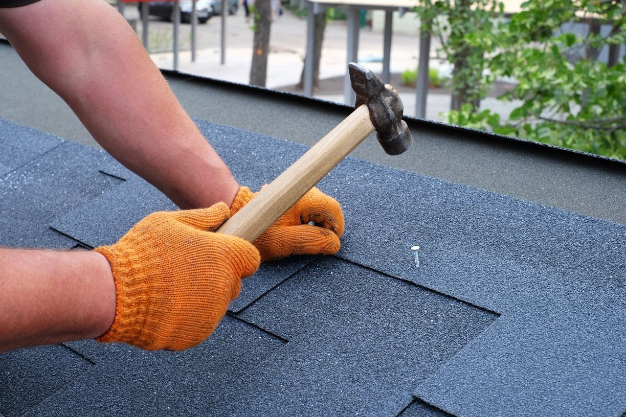 Gloved hands hammering roofing shingles on a rooftop
