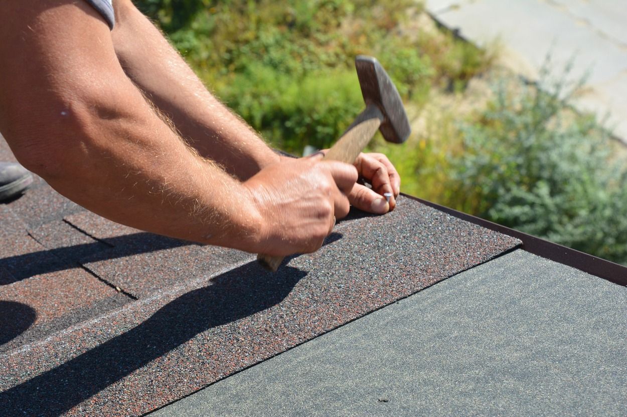 Person hammering roofing shingles on a roof during repair work