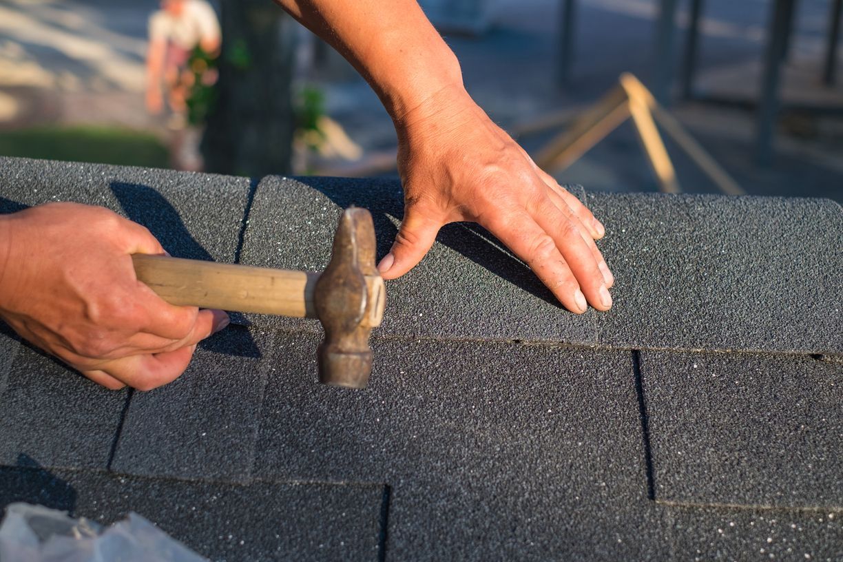 Hands hammering asphalt shingles during roof installation