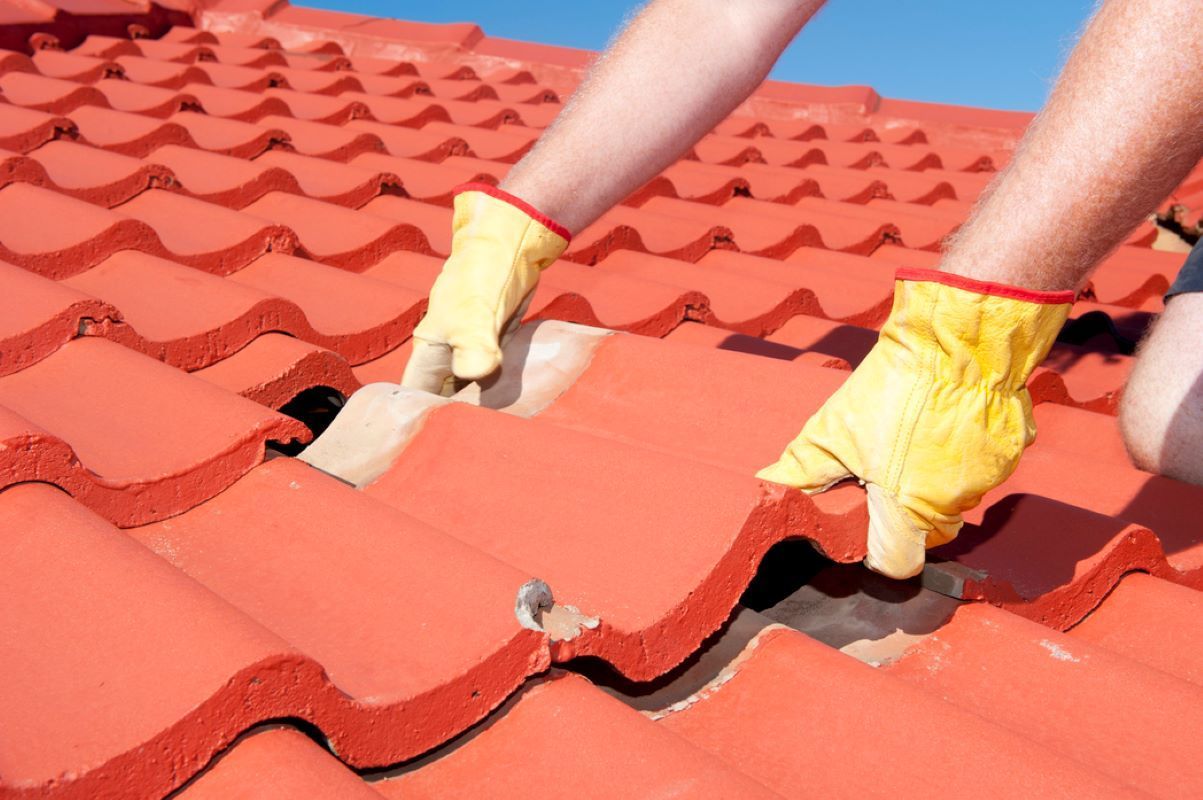 Hands in yellow gloves installing red roof tiles on a roof