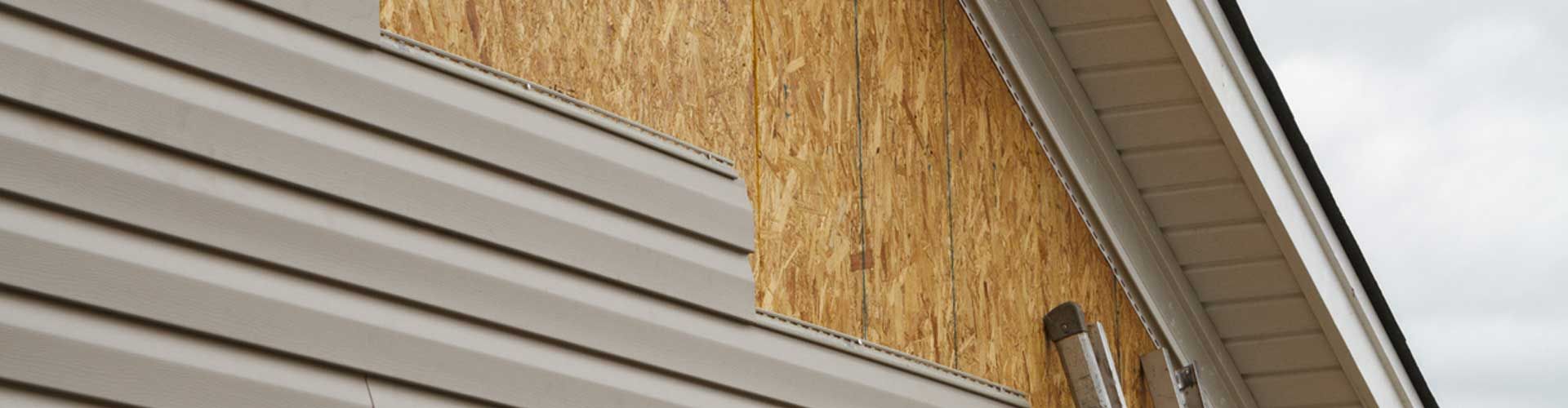 Side view of a house with tan siding and plywood sheathing under the roof eaves