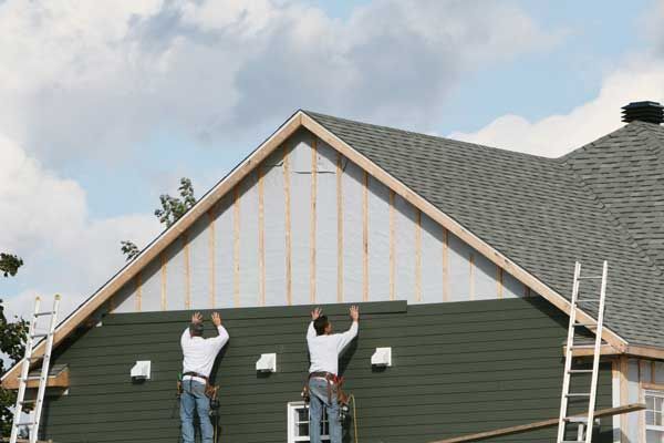 Two workers painting the exterior of a house under a cloudy sky