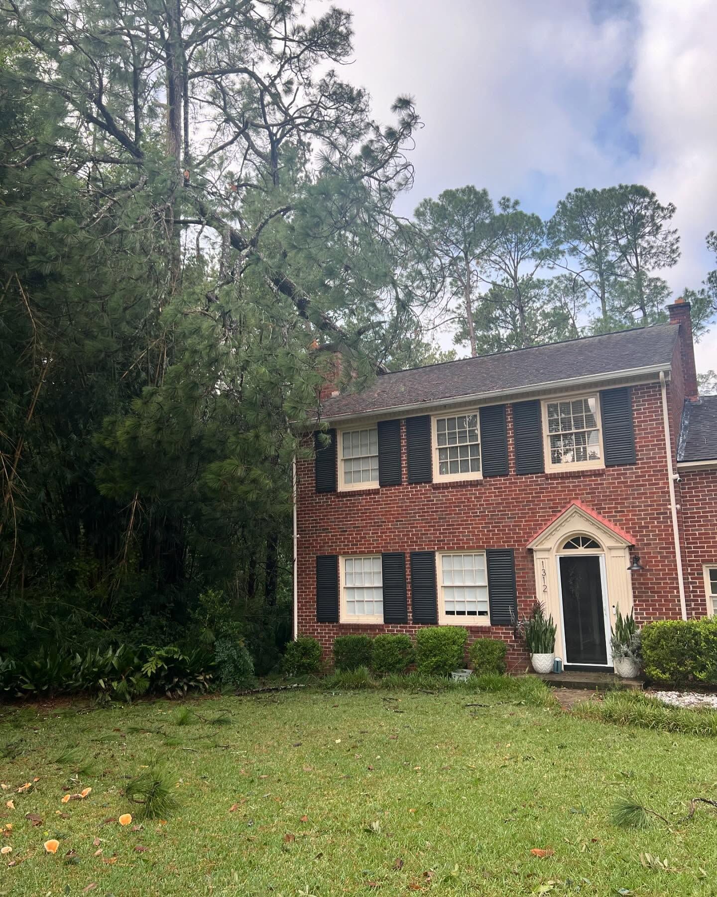 Two-story brick house with white trim and a green lawn, bordered by tall trees.