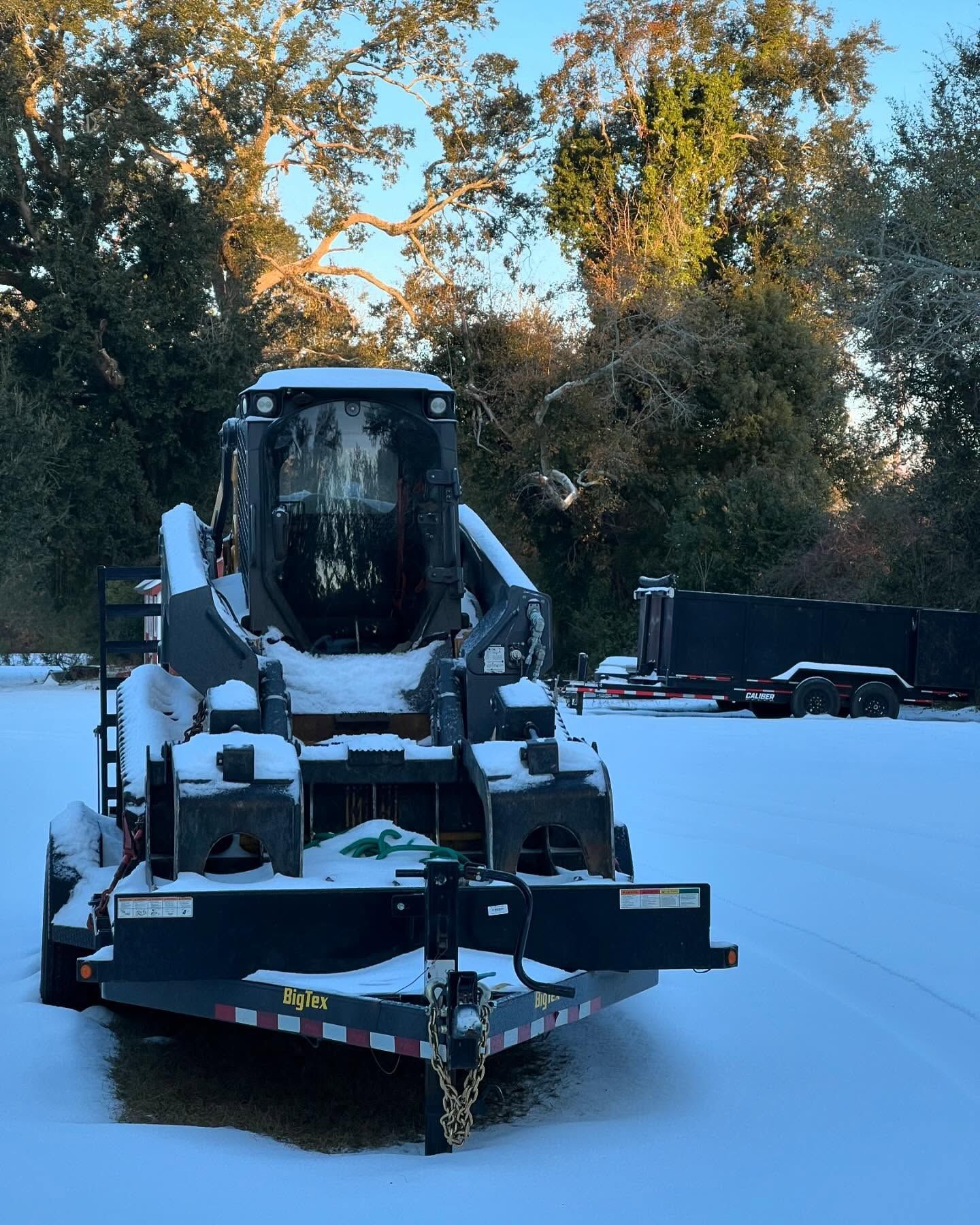 Snow-covered front loader in a snowy yard with trees in the background