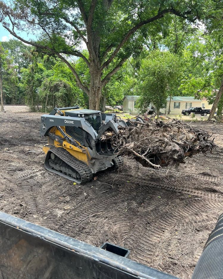 Yellow skid steer pushing a pile of brush in a wooded yard