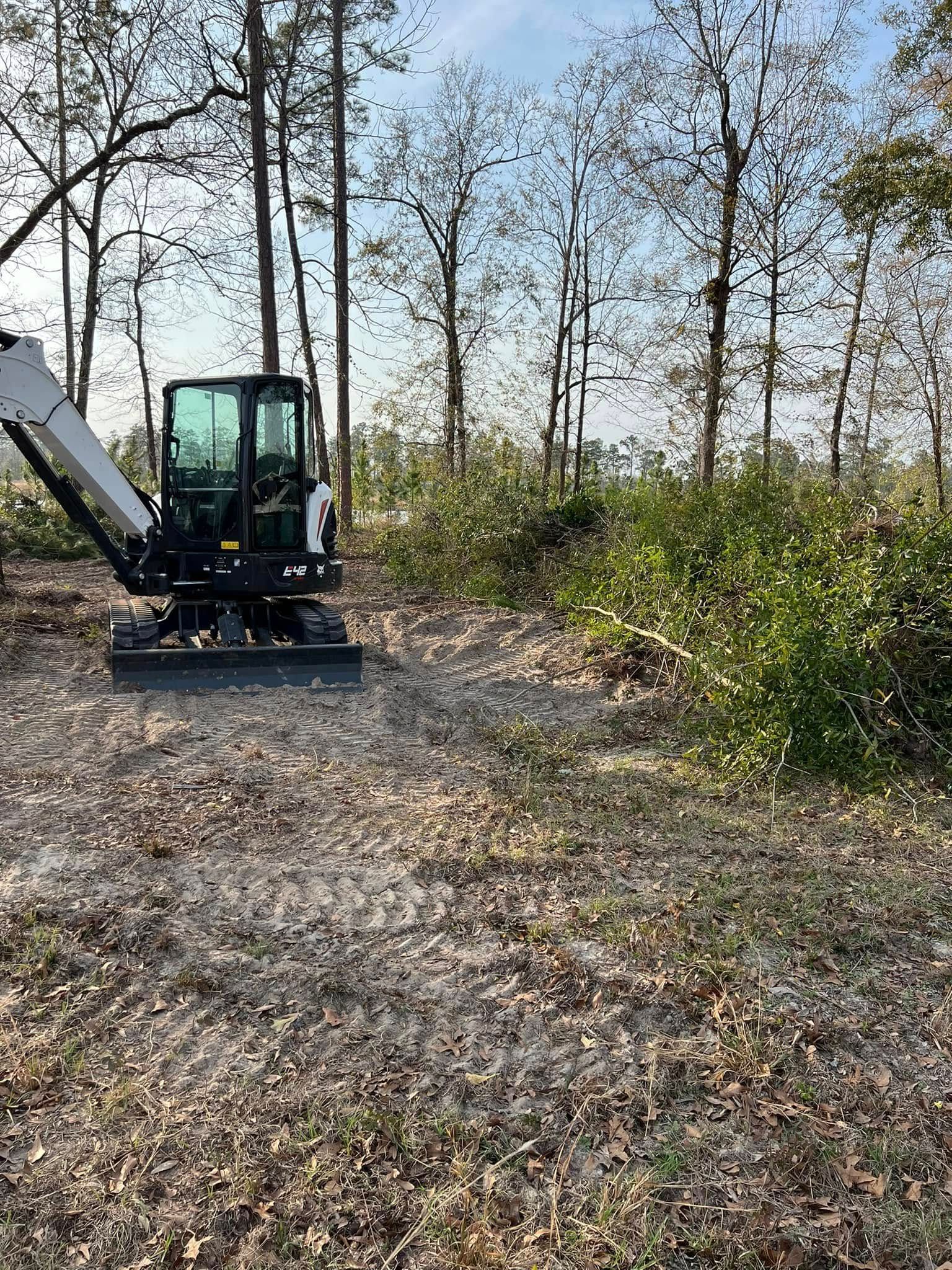 Small excavator in a wooded clearing with a gravel path and autumn trees