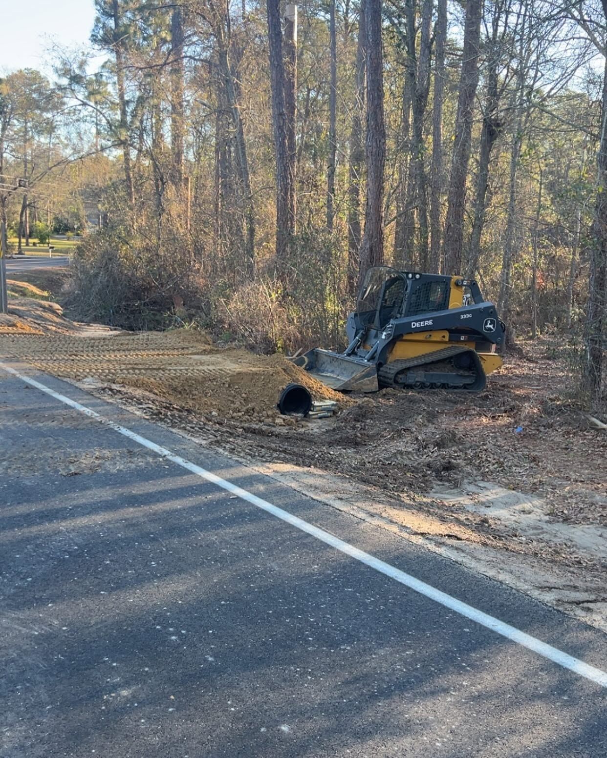 Small excavator by a roadside ditch beside trees in autumn.
