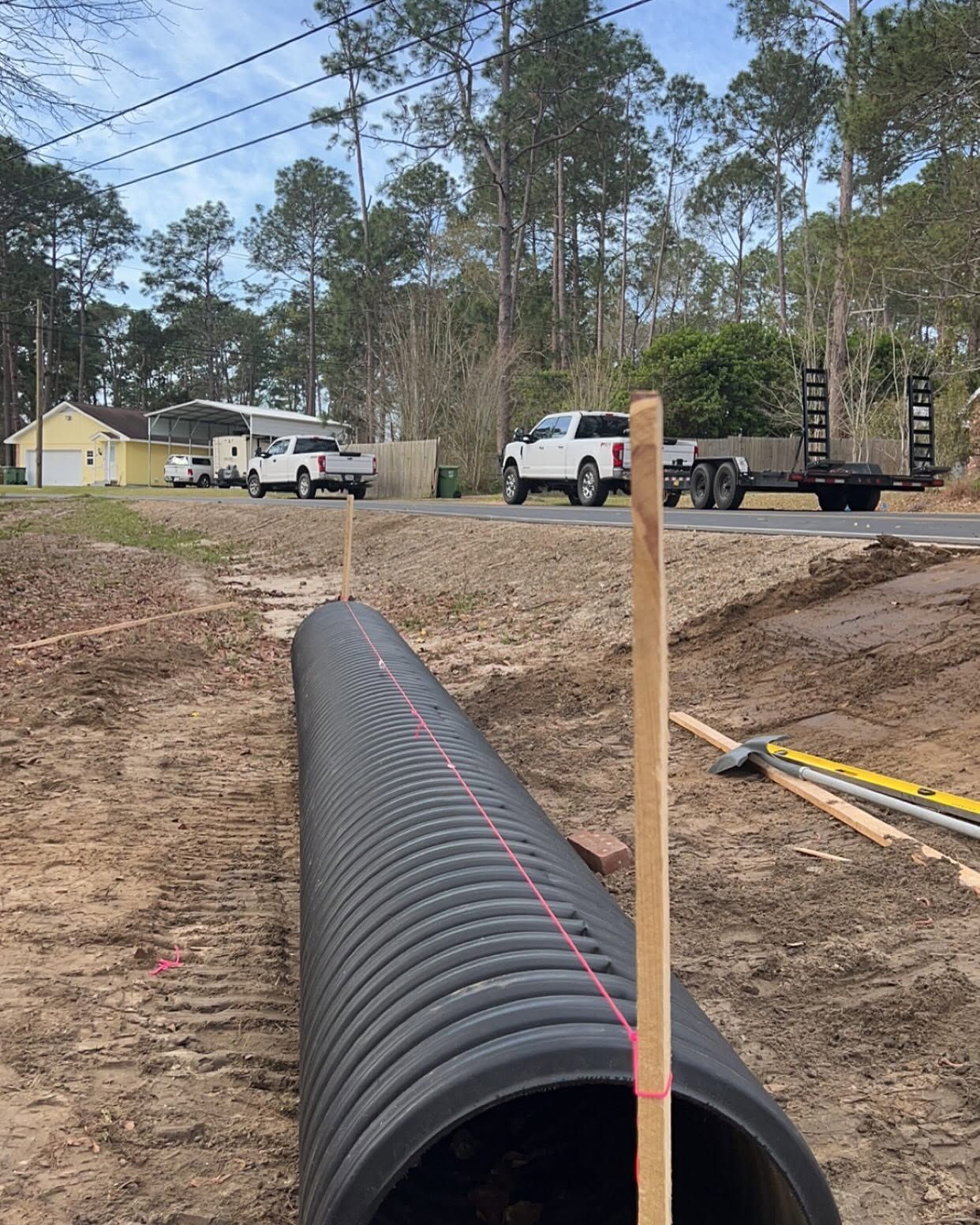 Black corrugated drainage pipe laid in a dirt trench at a construction site with trucks nearby