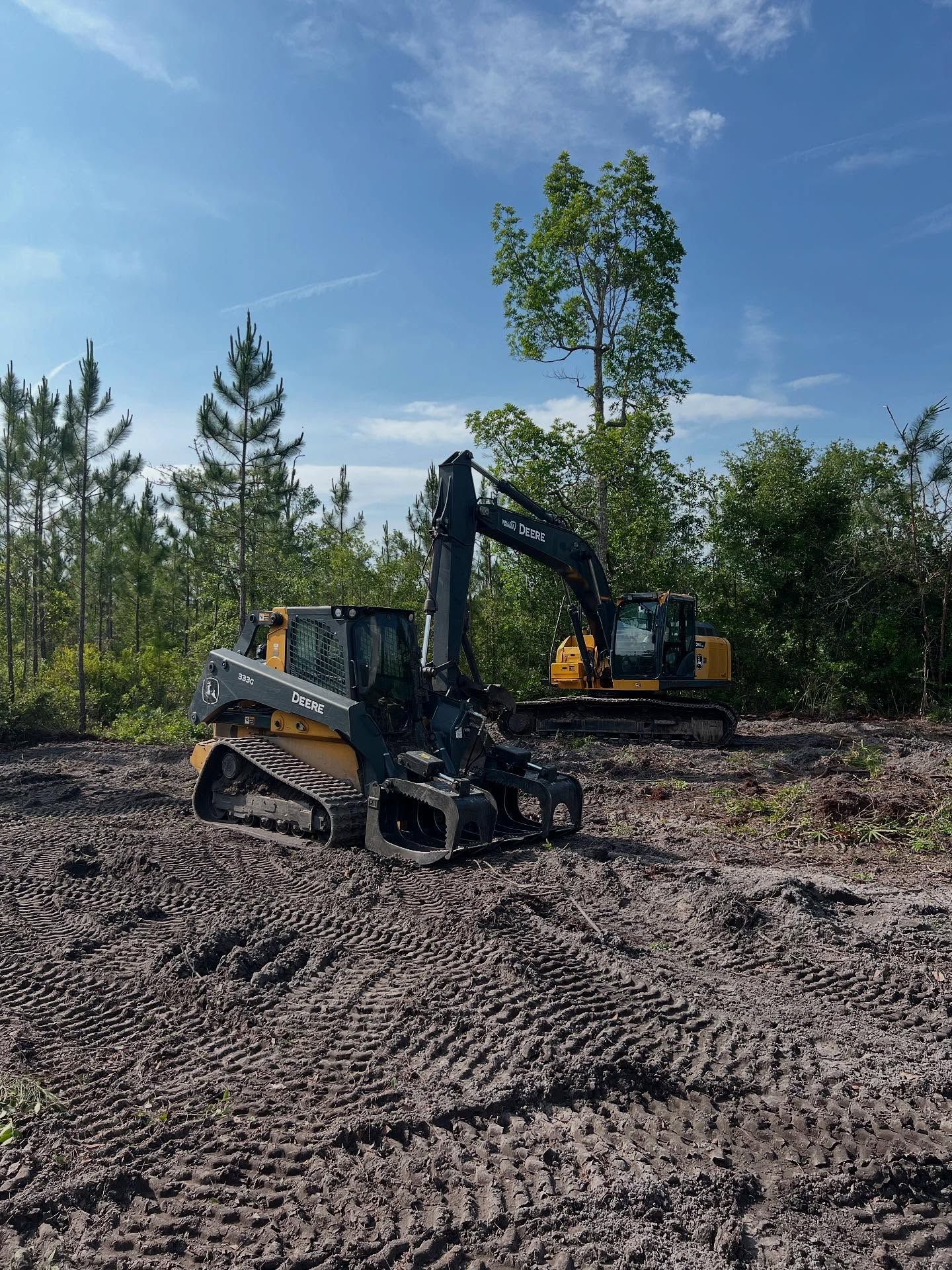 Yellow excavator and skid steer working on a dirt clearing under a blue sky