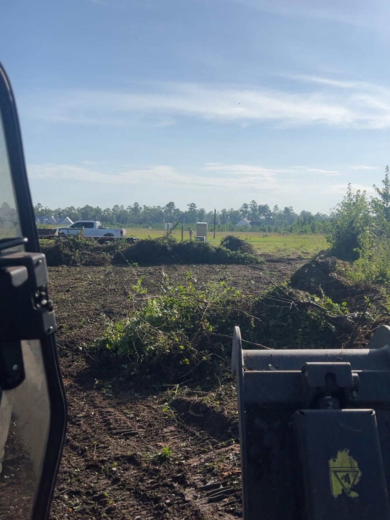 Sunny farm field with a tractor view, piles of vegetation, and trees in the distance