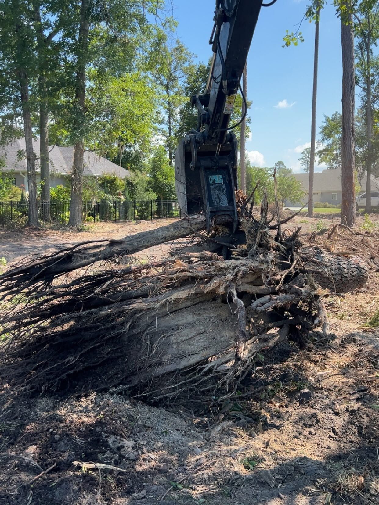 Excavator clearing burnt debris in a wooded area under a blue sky