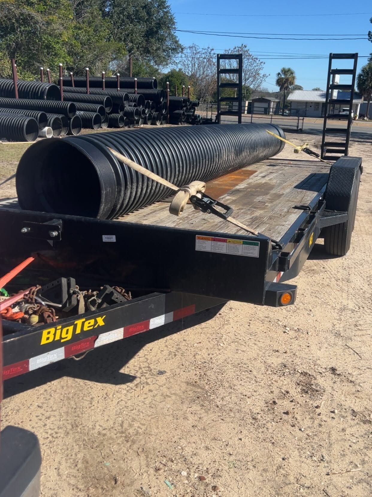 Black dump trailer carrying a large corrugated pipe on a sunny construction lot