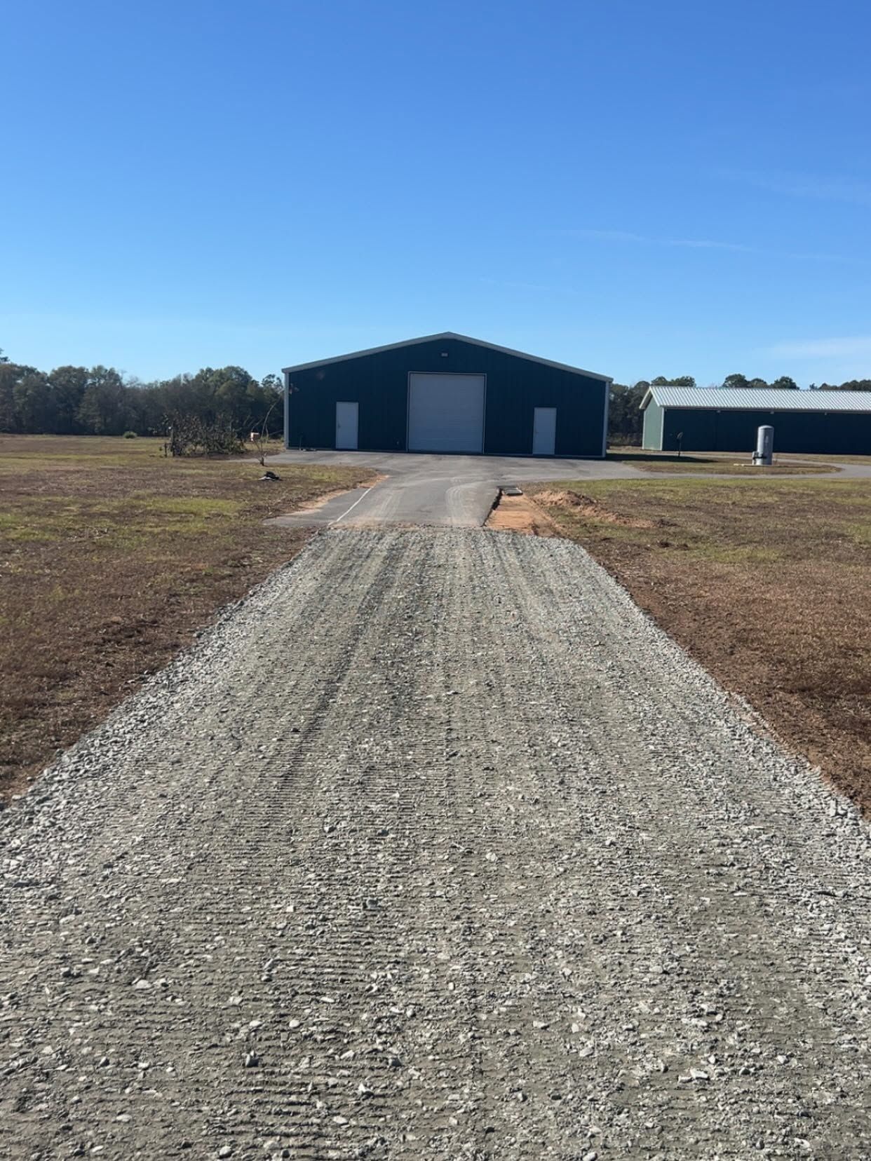 Gravel driveway leading to a dark blue barn with white doors under a clear blue sky