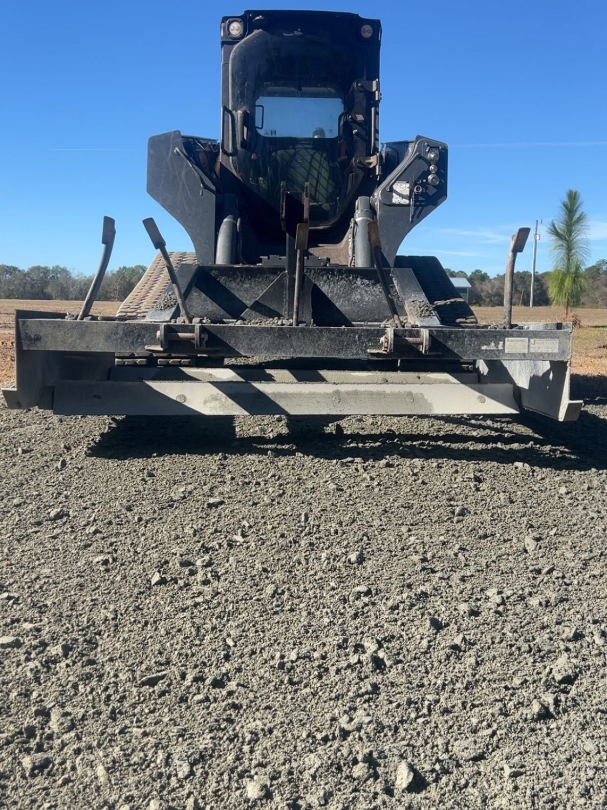 Large black skid steer with a front attachment parked on a gravel lot under a clear blue sky