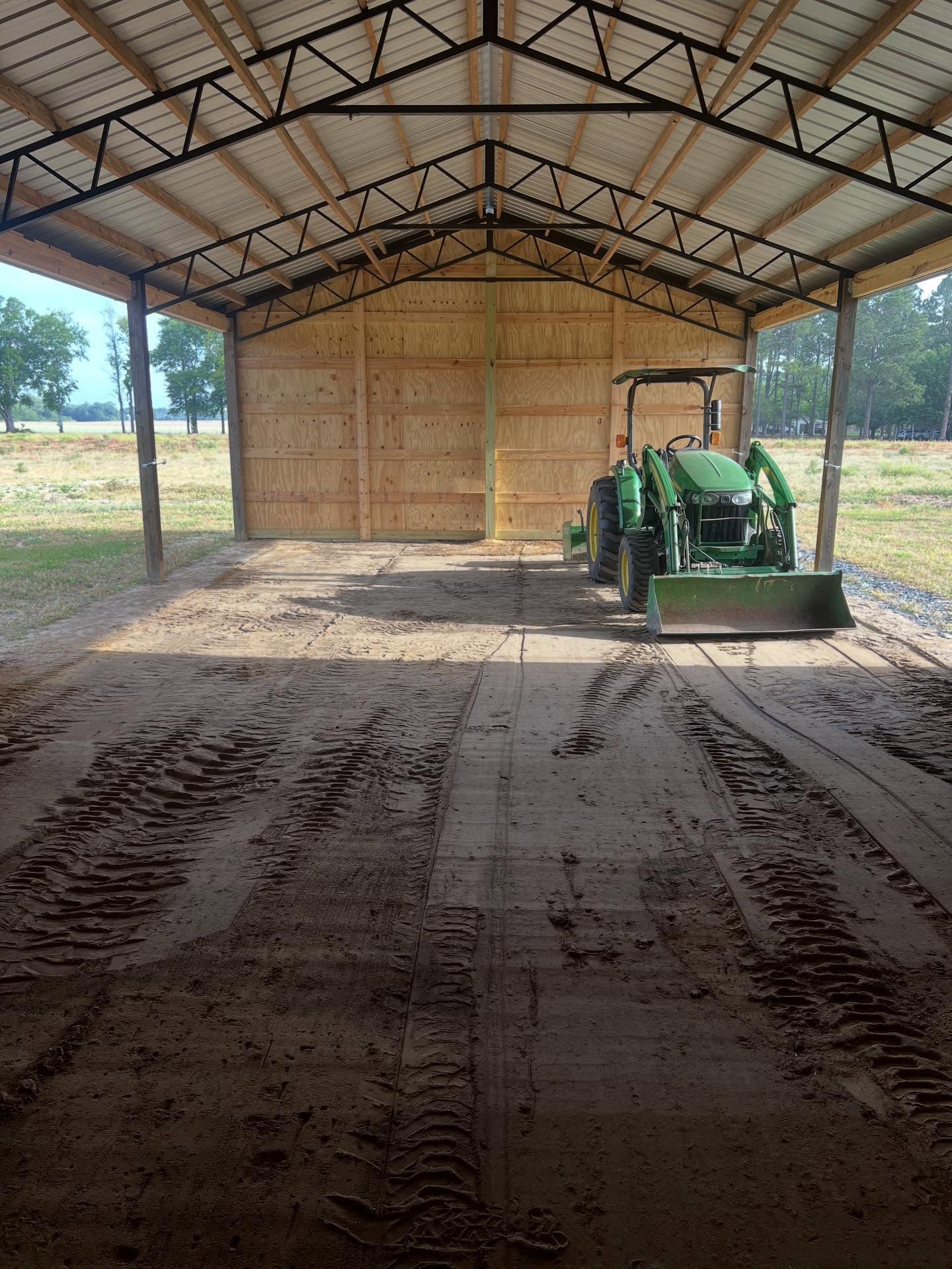 Covered farm shed with a green tractor inside and dirt tire tracks on the floor.