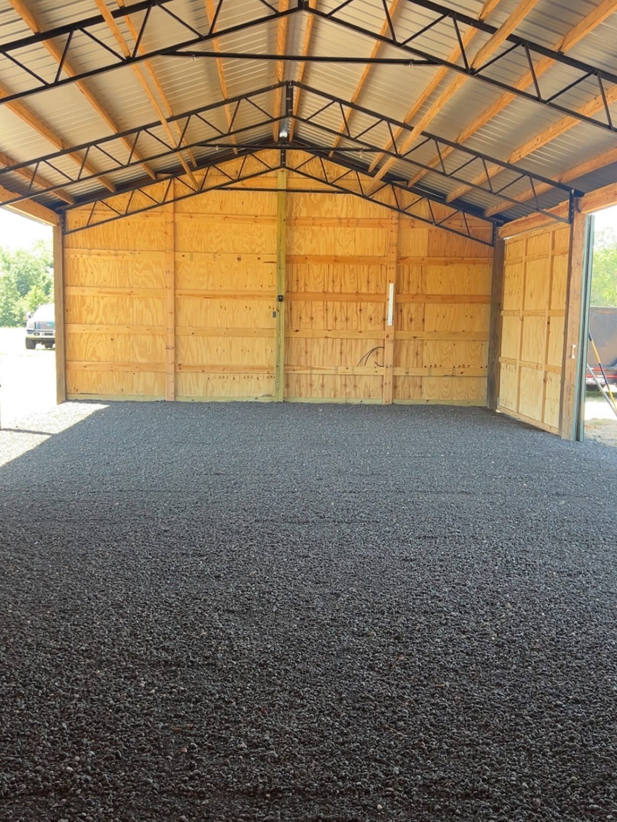 Empty wooden shed with a gravel floor and open front under a metal roof