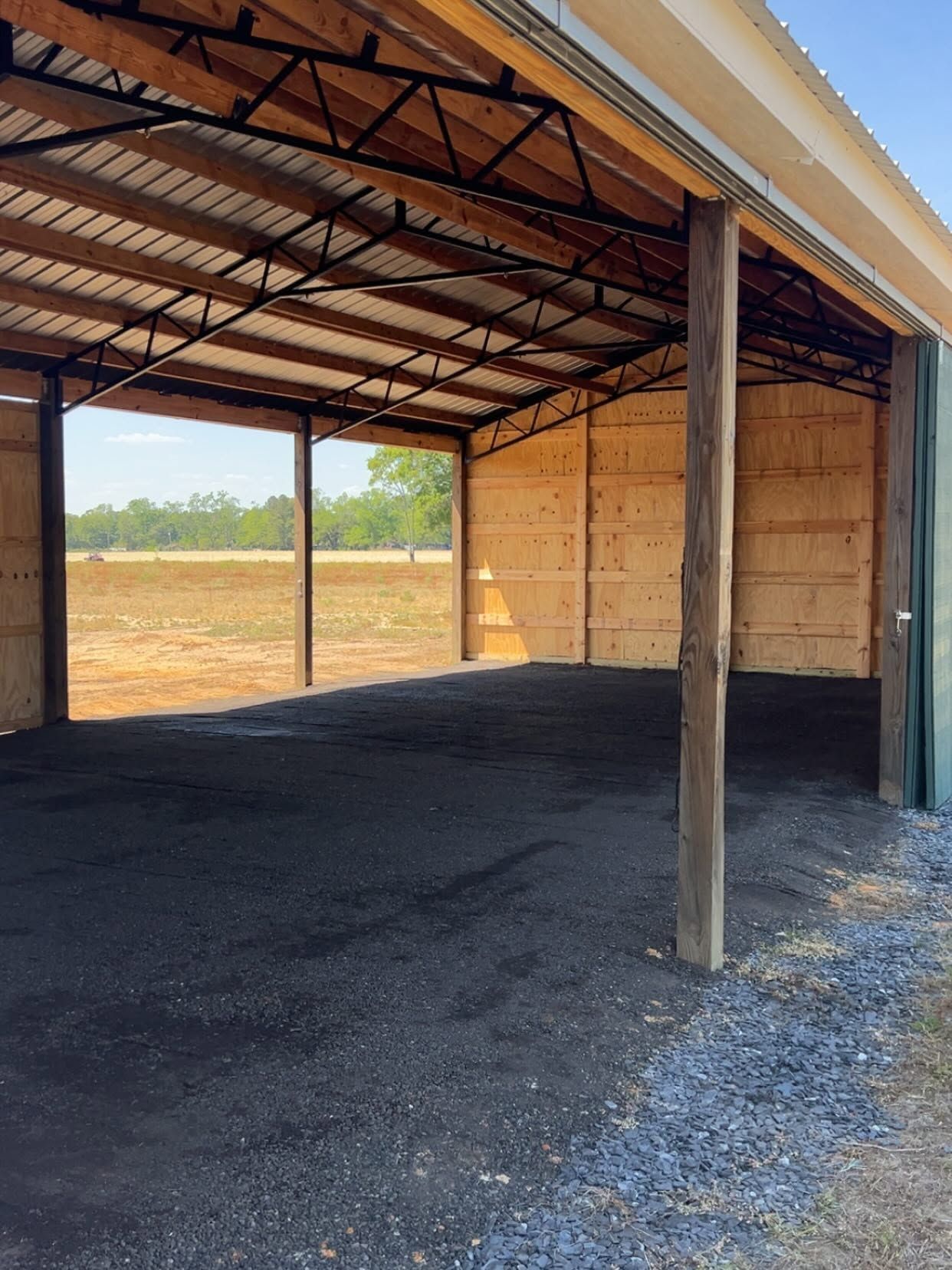 Empty open-sided metal shed with dirt floor and wooden walls, viewed from the entrance.