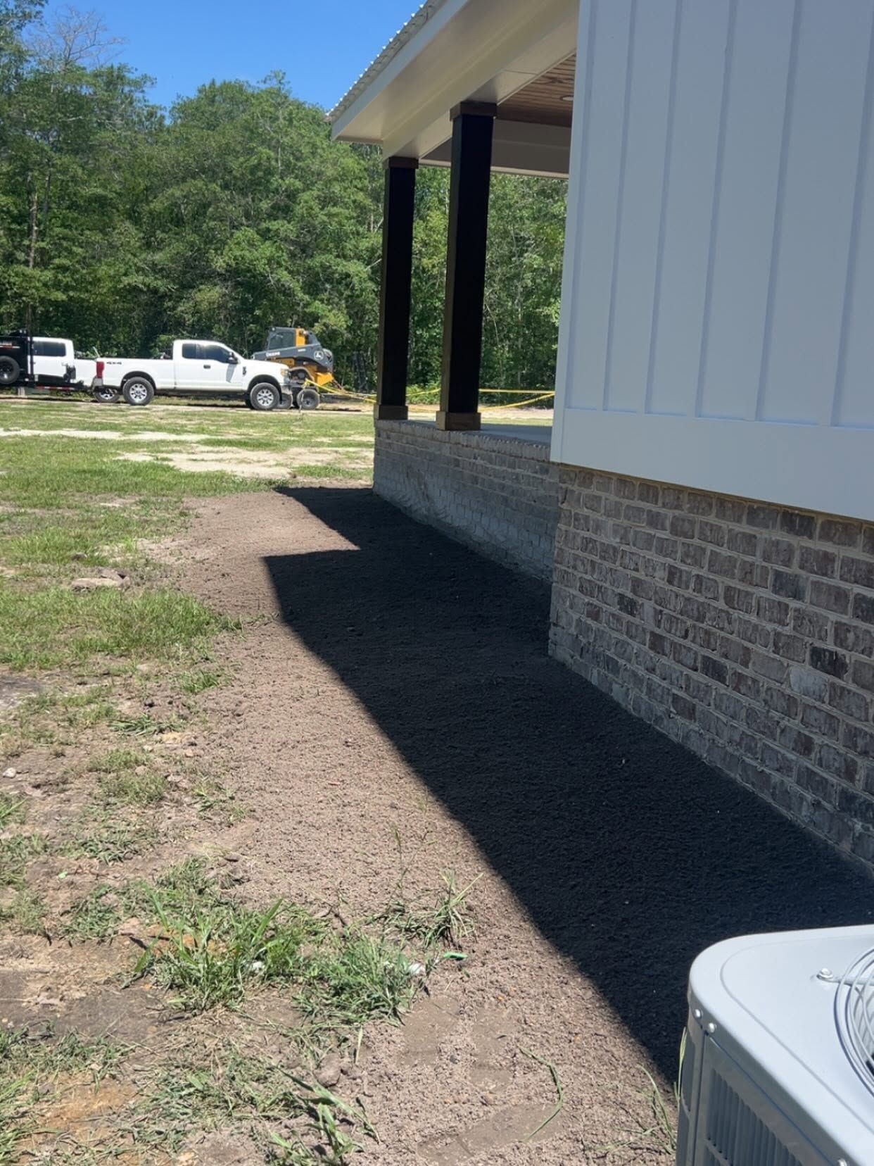 Side of a brick-and-siding building with a shaded walkway, gravel lot, and parked trucks in the background.