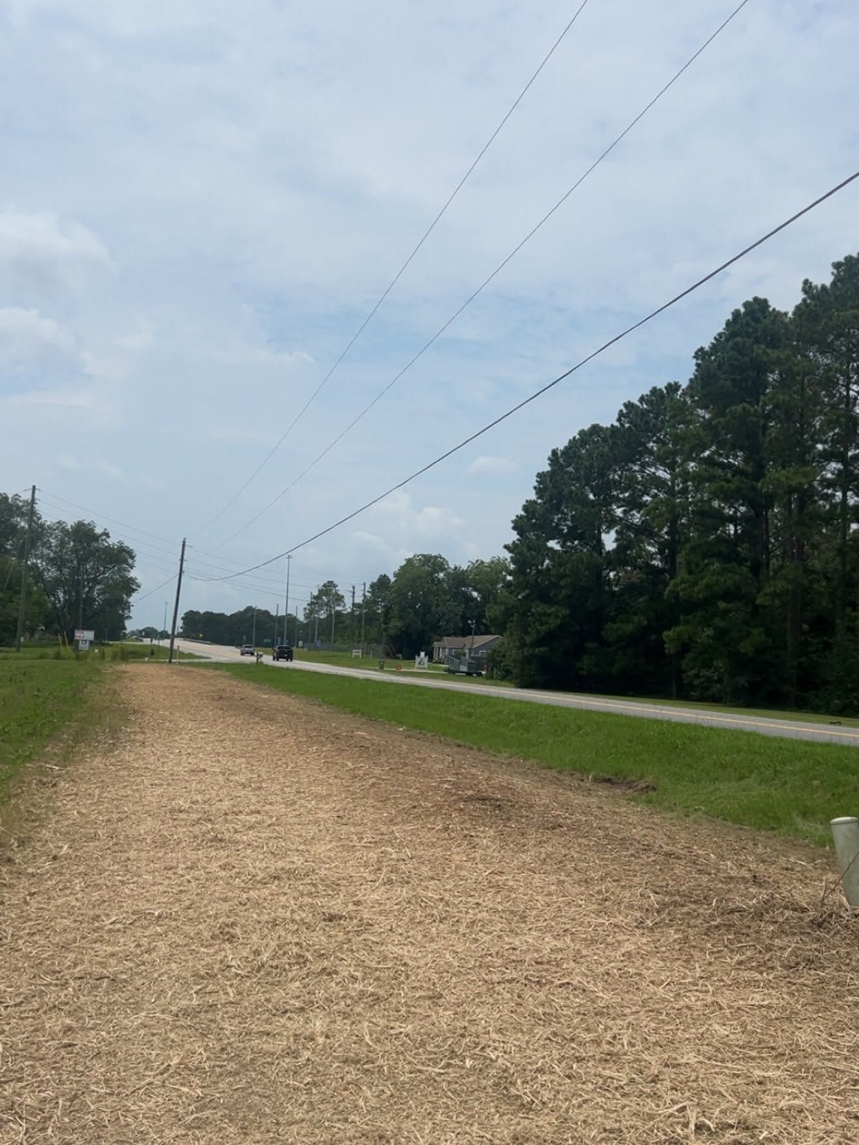 Gravel path beside a road under a cloudy sky, lined with trees and power lines